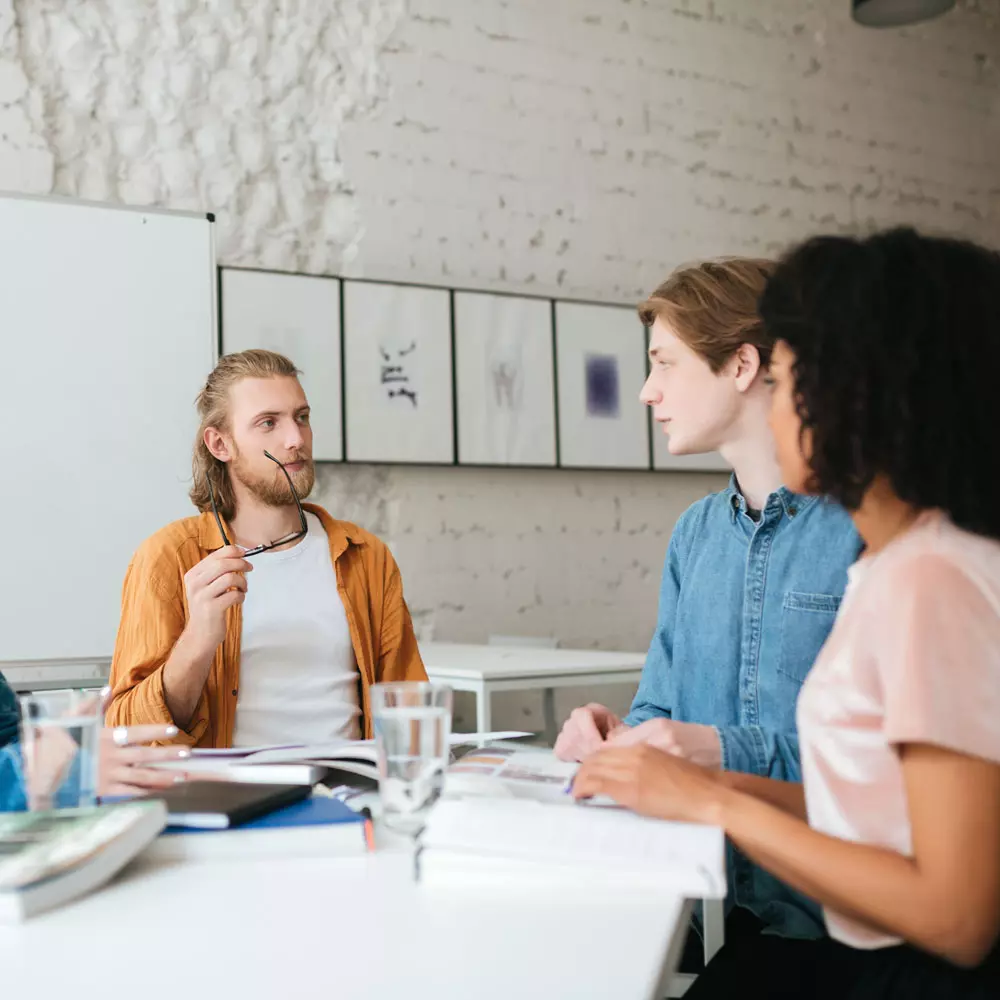 Lees meer Vier collegas zitten rond een tafel in een ruimte met witte bakstenen muren en afbeeldingen aan de muur.